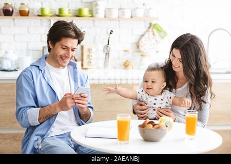 Millennial man texting on phone, dining with wife and baby Stock Photo