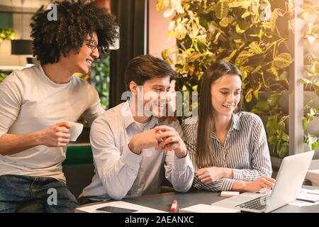 Millennial partners reading great news on laptop, dining in cafe Stock Photo