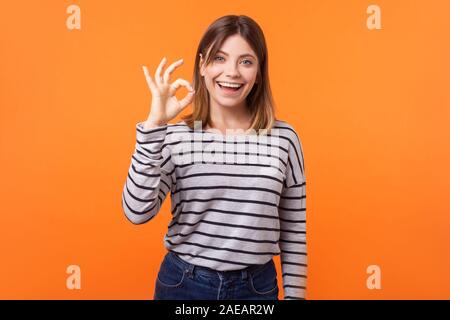 I am ok! Portrait of satisfied beautiful young woman with brown hair in long sleeve striped shirt standing showing okay gesture with fingers, good job Stock Photo