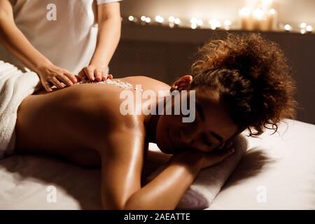 Spa treatment. Beauty therapist pouring salt scrub on womans back Stock Photo