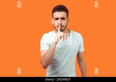 Shh, make silence please! Portrait of serious brunette man with beard in white t-shirt standing showing quiet gesture, saying hush, keep secret. indoo Stock Photo