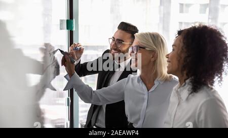 Smiling diverse colleagues brainstorm writing on whiteboard Stock Photo