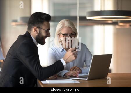 Smiling multiracial colleagues brainstorm using laptop at meeting Stock Photo