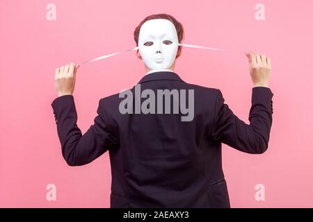 Businessman in black suit standing with his back turned to camera and covering head with mask, hiding identity. business fraudulence, lie in partnersh Stock Photo