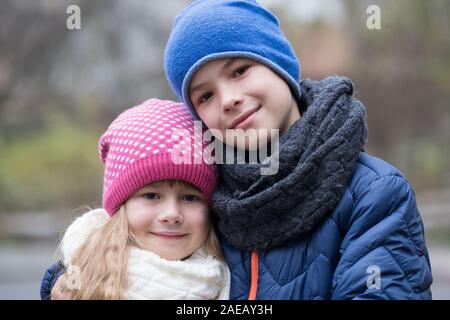 Two children boy and girl hugging each other outdoors wearing warm clothes in cold autumn or winter weather. Stock Photo