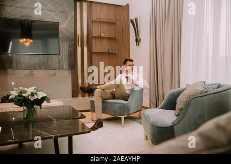 Young man sits in a luxury apartment, drinking red wine and and relaxing Stock Photo