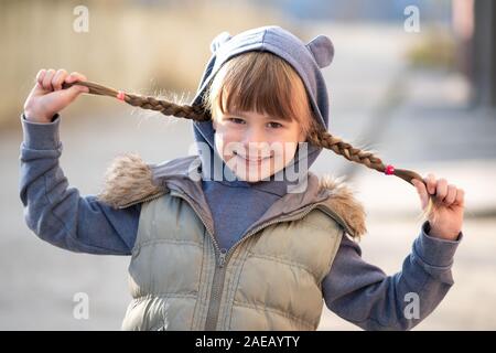 Portrait of happy child girl with hair braids in warm clothes in autumn outdoors. Stock Photo