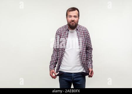 Portrait of bankrupt bearded man in casual plaid shirt standing upset with depressed face expression, turning out empty pockets has no money, low sala Stock Photo