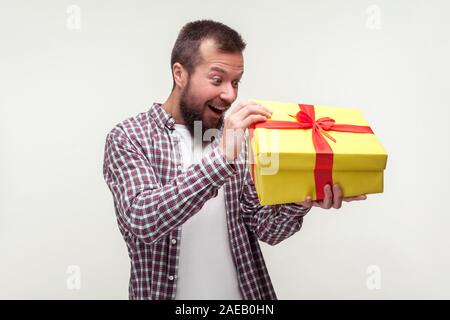 Portrait of excited surprised bearded man in casual plaid shirt unpacking big present, looking amazed pleasantly surprised with what's inside birthday