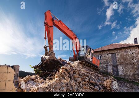 A heavy industrial work machine, digger is destroying an abandoned old building. Stock Photo