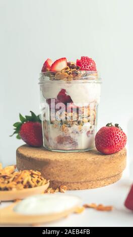 a jar with tasty parfaits made of healthy granola, strawberries and Greek yogurt on white background. Shot at angle. Stock Photo