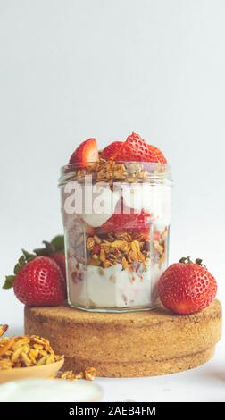a jar with tasty parfaits made of healthy granola, strawberries and Greek yogurt on white background. Shot at angle. Stock Photo