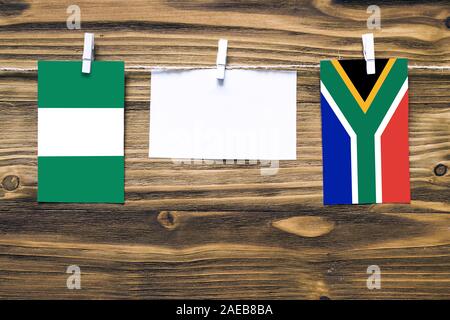 Hanging flags of Nigeria and South Africa attached to rope with clothes pins with copy space on white note paper on wooden background.Diplomatic relat Stock Photo