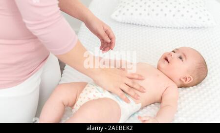 Mother standing next to bed with her newborn baby boy lying on his back. Baby boy on a bed wearing a nappy looking at the mother and smiling. Stock Photo
