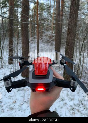 Man hand holding bright red drone to be lift up in a snow forest in Baltics Riga Latvia - Cold snow trees in the background Stock Photo