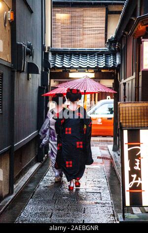 Two geisha / maiko walking down a narrow back alley holding a rice paper parasol in rainy Gion district, Kyoto, Japan Stock Photo