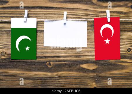 Hanging flags of Pakistan and Turkey attached to rope with clothes pins with copy space on white note paper on wooden background.Diplomatic relations Stock Photo