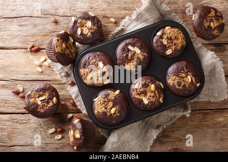 Dark chocolate vegetarian muffins with peanut butter and nuts in a baking dish on the table. Horizontal top view from above Stock Photo