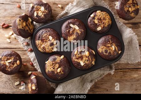 Homemade chocolate muffins with peanut butter and nuts in a baking dish on the table. Horizontal top view from above Stock Photo