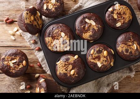 delicious breakfast of chocolate muffins with peanut butter and nuts in a baking dish on the table. Horizontal top view from above Stock Photo