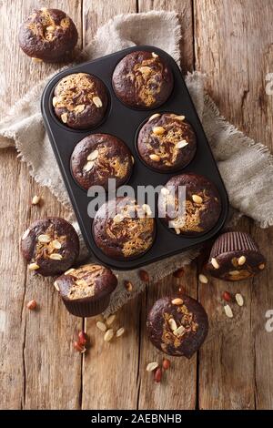 Freshly baked chocolate muffins with peanut butter and nuts in a baking dish on the table. Vertical top view from above Stock Photo