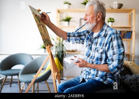 Handsome mature man artist paints on canvas painting on the easel Stock Photo
