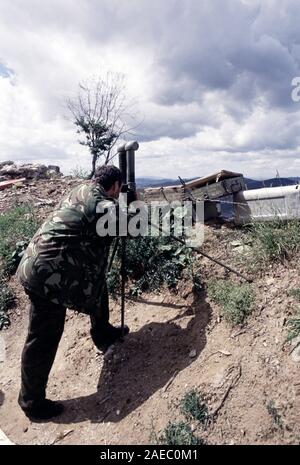 11th August 1993 During the Siege of Sarajevo: a Bosnian-Serb soldier uses WW2 trench binoculars to view the city below, next to his bunker on Mount Trebevic. Stock Photo