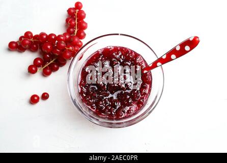 Homemade jam. Top view of red currant jam in a glass bowl and fresh currant on white background. Stock Photo