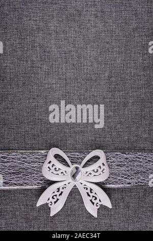 Beautiful shiny tied white glitter bow on silver colored ribbon and on gray natural textured burlap. Bow and ribbon are at the bottom of image. Vertic Stock Photo
