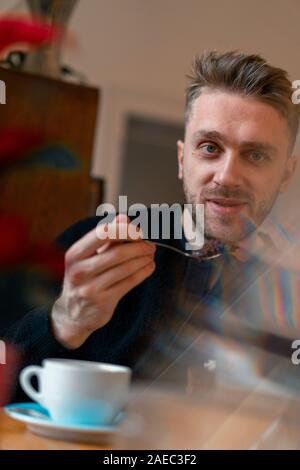 Young Handsome Man Drinking Hot Tea And Eating Cinnamon Cake After Strolling At Christmas Market In Cozy Cafe Stock Photo