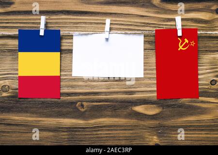 Hanging flags of Romania and Soviet Union attached to rope with clothes pins with copy space on white note paper on wooden background.Diplomatic relat Stock Photo