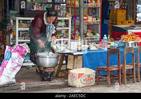 Local woman draws soup into a bag at a small food stall, Luang Prabang, Laos Stock Photo