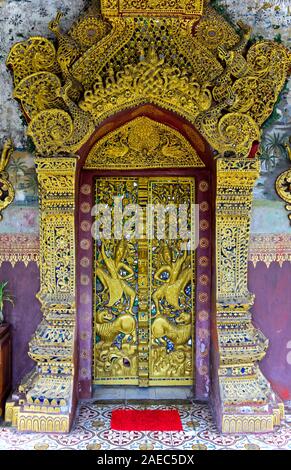 gilded wooded door panels in bas-releif depicting Rama fighting mythical lions, Temple Wat Pa Phai, Luang Prabang, Laos Stock Photo