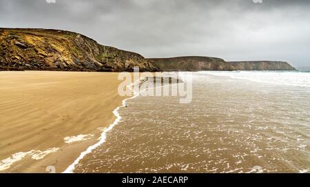 Sandy beach in winter in Brittany. The waves of the ocean come to die on the deserted beach under a gray sky laden with rain Stock Photo