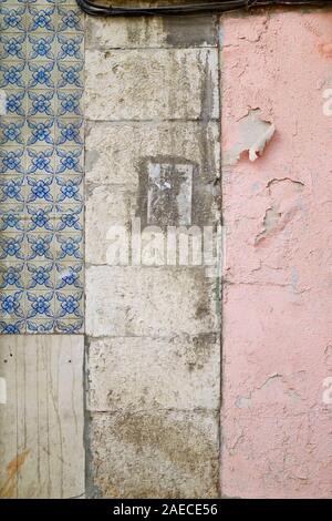 Front view of an old wall with faded blue ceramic tiles (azulejos), dirty and weathered stone blocks and pink paint peeling off. Textured background Stock Photo