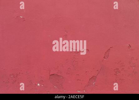 Close-up of a weathered red concrete wall with holes in the plastering and paint peeled off. High resolution abstract full frame textured background. Stock Photo