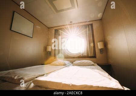 Ship Cabin With Bed And Window With View On Sea. Luxury Cabin On Ferry Boat Or Cruise Liner. Sunset Sun Shine Through Ship Porthole Window. Stock Photo
