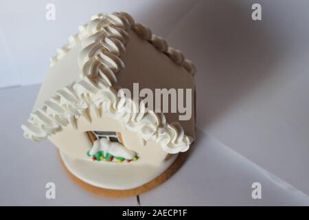 Photo of a ginger santa cookie house with a candle inside on the white creme background. Christmas decoration Stock Photo