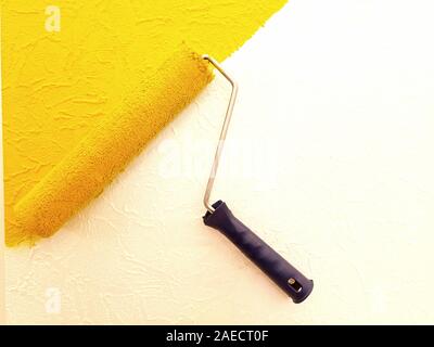 The texture of the wall is painted in bright colors. The wall is painted yellow and white with a painting tool. Nearby lies a painting tool - a roller Stock Photo