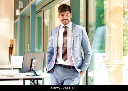 Portrait of confident young businessman wearing suit and tie while relaxing in the office window. Stock Photo