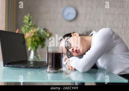 Tired overworked woman sleeping at desk in office, coffee does not help Stock Photo