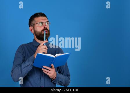 Man with beard and book. Idea and knowledge concept. Professor with thinking face. Teacher wears glasses and holds organizer. Textbook and pen in guys hands on blue background, copy space Stock Photo