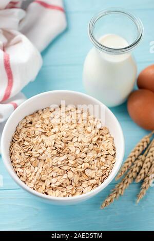 Oats, oat flakes and bottle of milk on blue background. Healthy breakfast food concept, diet food Stock Photo