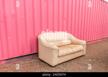 old cream leather sofa or settee or couch against pink corrugated metal siding in Alamogordo, New Mexico, United States historic Route 66 Stock Photo