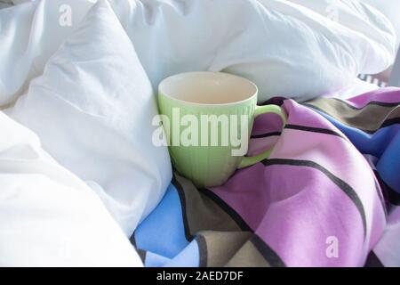 Green cup in bed with white blanket and striped duvet Stock Photo