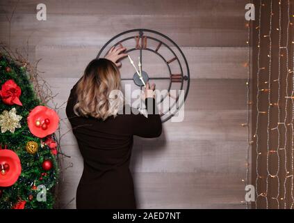 Young woman holding standing near the clock showing nearly 12. setting time on the wall Stock Photo