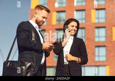 Businessman and businesswoman are talking on the phone while standing outdoors. Stock Photo