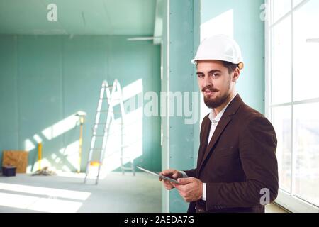 Foreman bearded man in a white helmet in a room at a construction site. Stock Photo