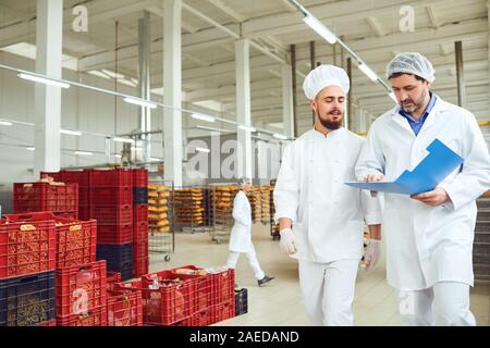 The technologist and baker speak in a bread factory. Factory workers in the workplace. Stock Photo