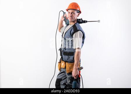 A builder with a hammer drill on his shoulder, in a helmet, smiles. Stock Photo